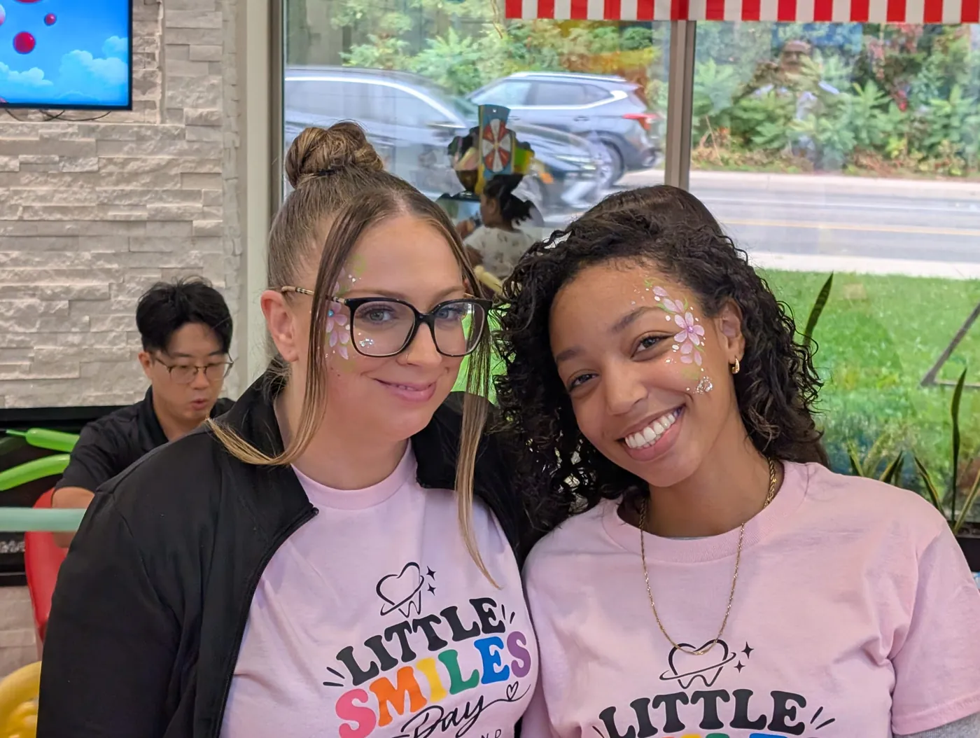 Two Heartland team members in Little Smiles Day shirts smiling with glitter face paint