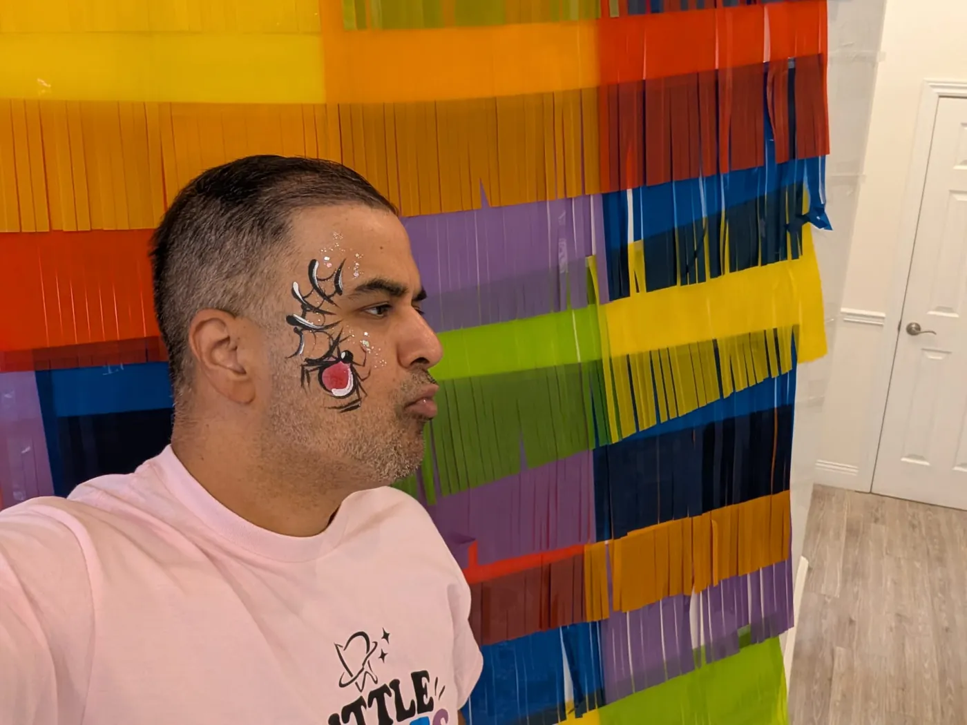 Smiling man with spider-web face paint in front of a colourful streamer backdrop