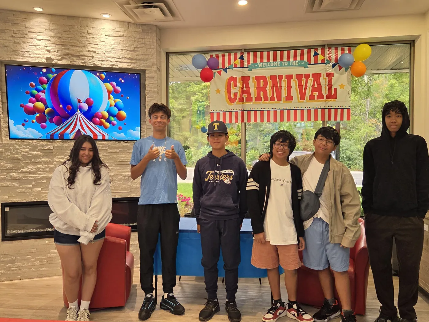 Group of kids and teens posing in front of the Little Smiles carnival banner in the Heartland waiting area